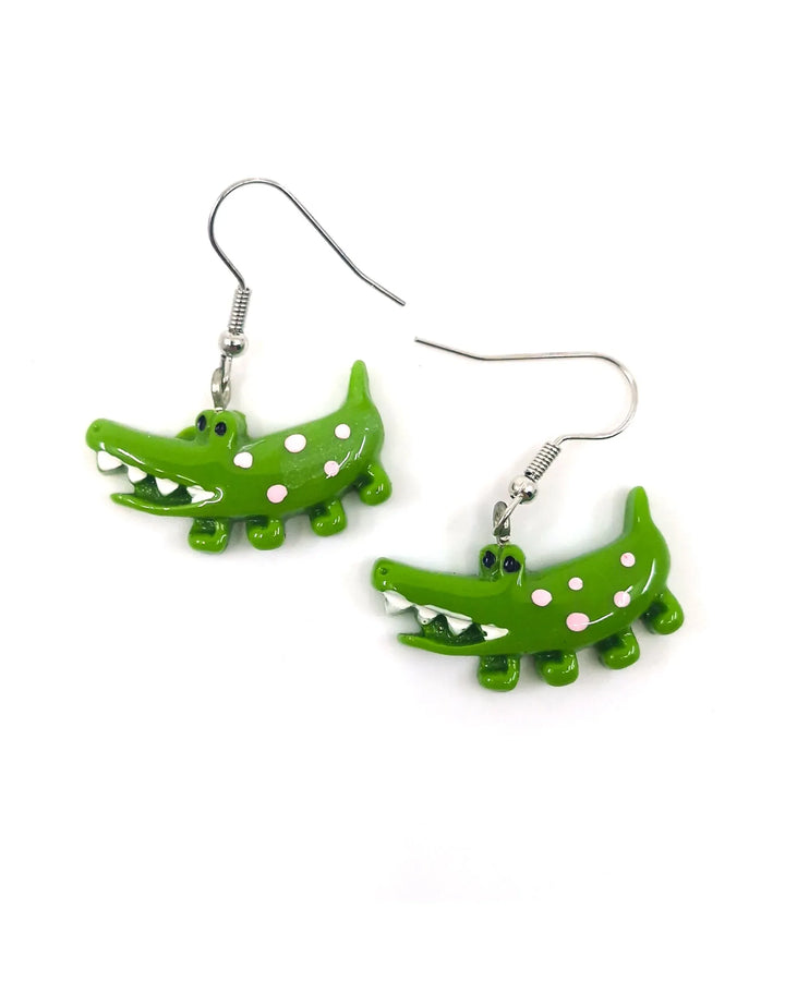Front view of bright green crocodile dangle earrings with pink and white spots and silver hooks on a white background.