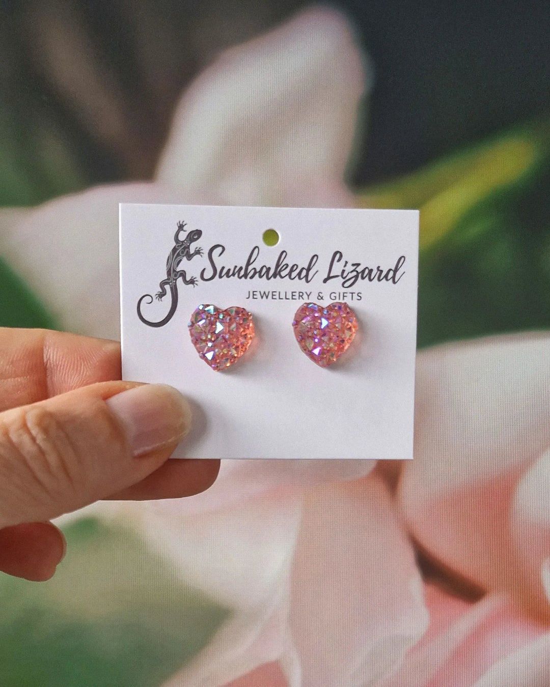 Sparkly heart shaped earrings in pale pink with pink flowers in the background