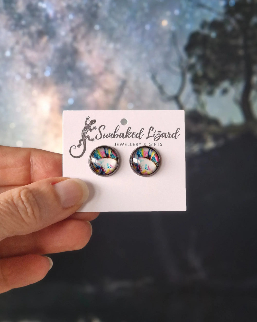 Abstract rainbow stud earrings styled against a starry sky background with swirling colours