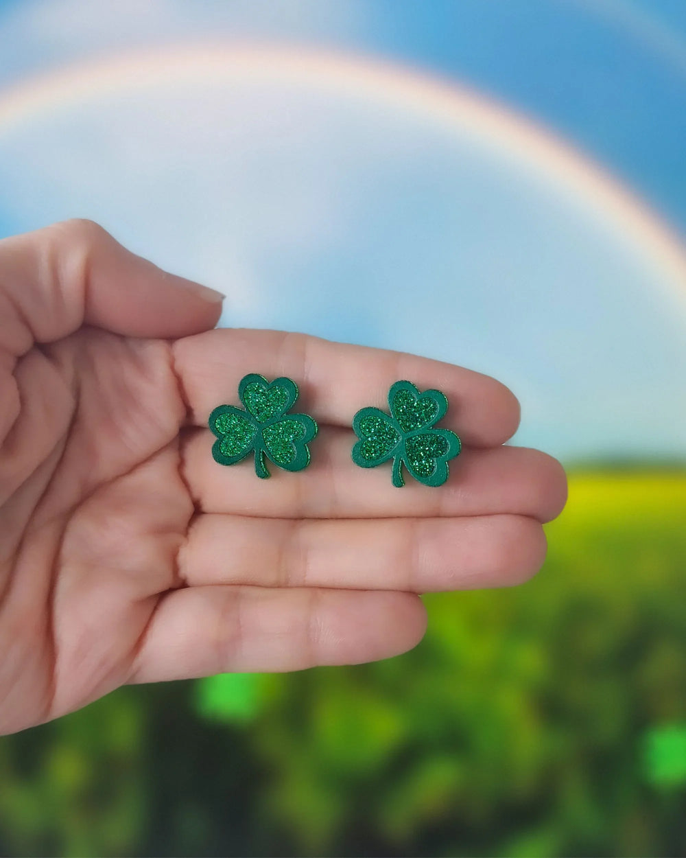 Green glitter shamrock stud earrings resting on hand, showing small size and sparkly finish