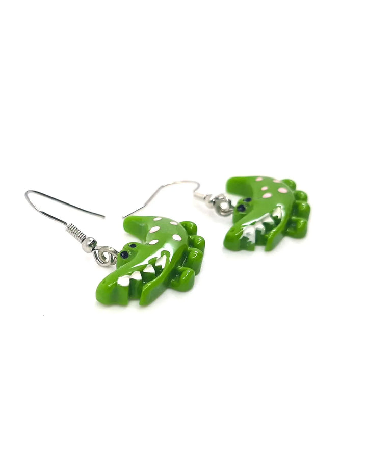 Angled close-up of bright green crocodile dangle earrings with white spots and silver hooks on a white background.
