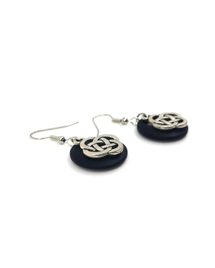 Close-up of silver-tone Celtic knot charm on black timber backing