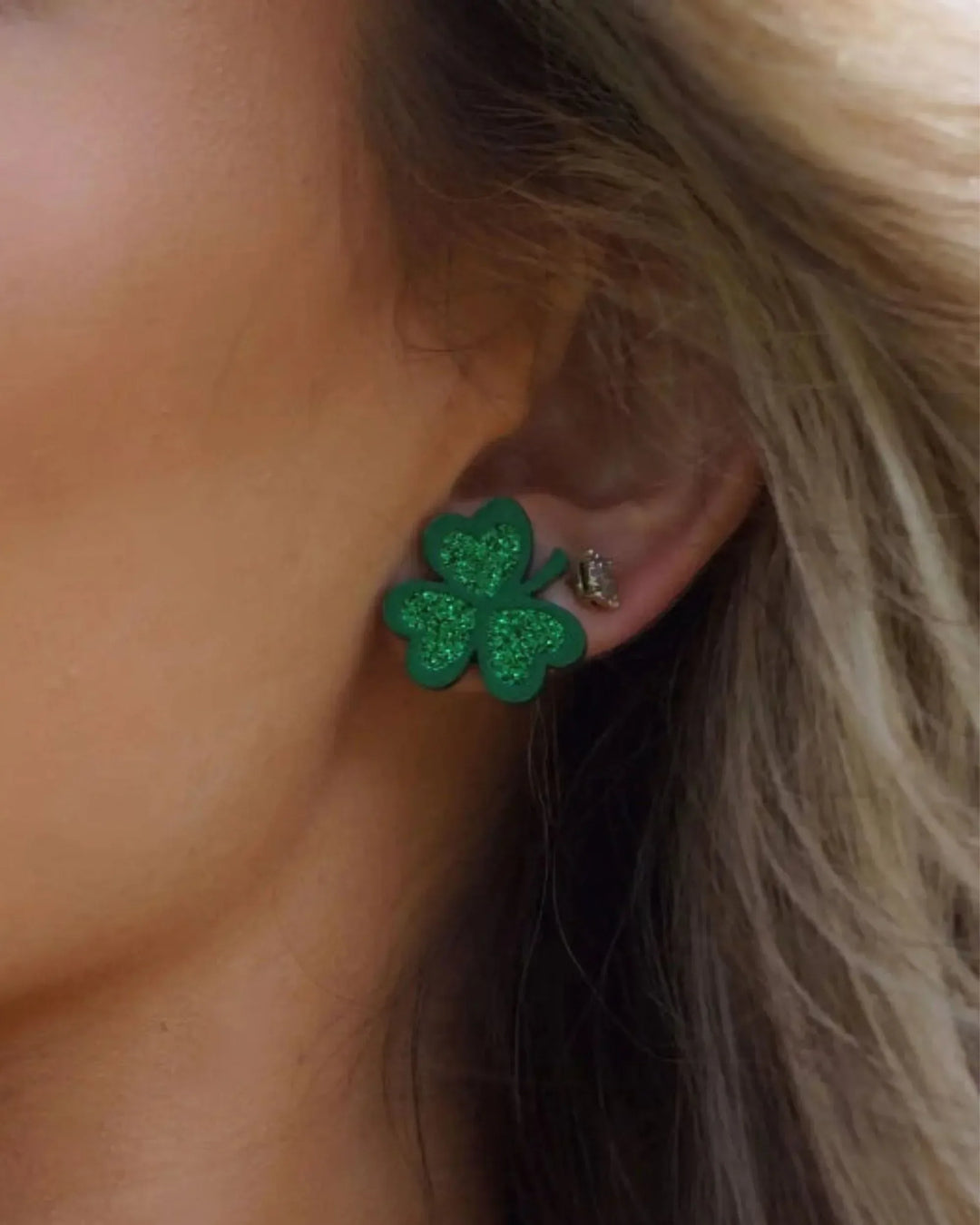 Close-up of green glitter shamrock stud earring worn on ear, showing 19 mm size and clover shape