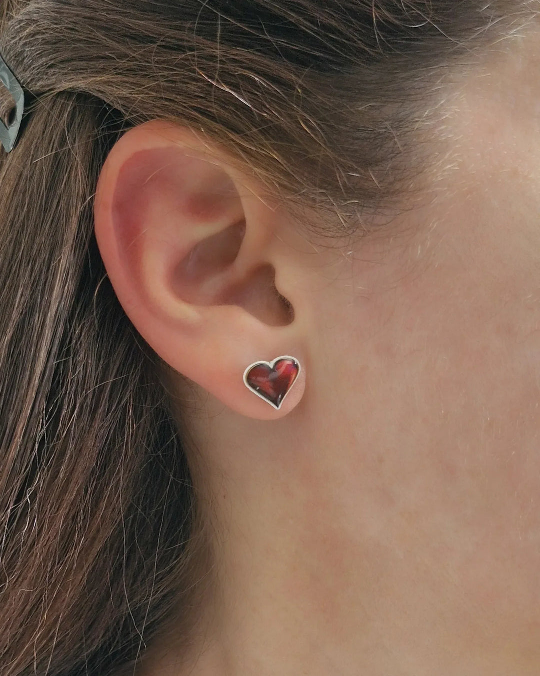 Shiny red heart stud earrings worn in ear, showing size and everyday fit