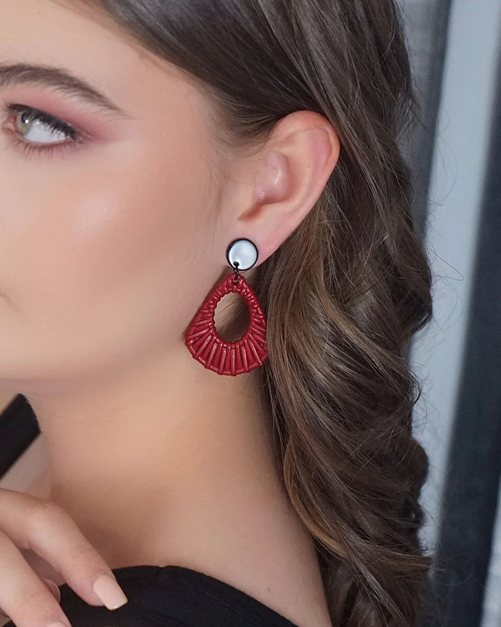 Close-up of red acrylic woven stud drop earrings worn on ear with black round stud top