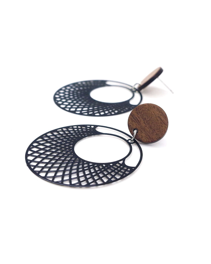 Side view of black filigree round earrings with timber stud top and cut-out lattice circle drop on white background