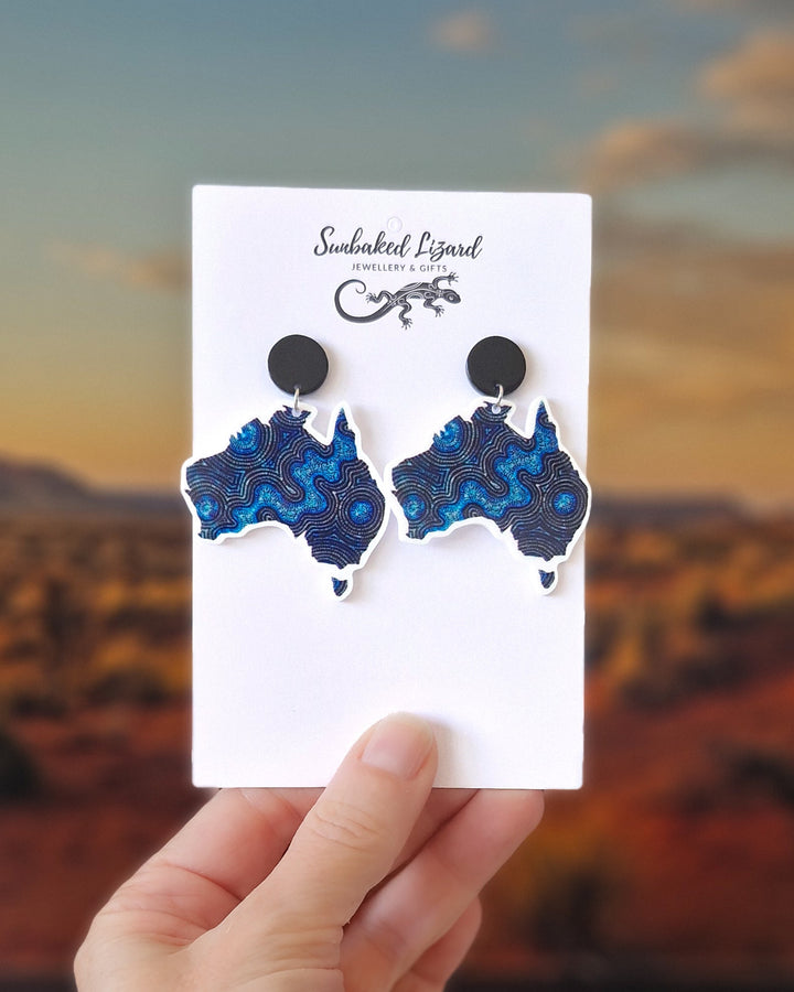Blue Dreamscape Australia map earrings featuring swirling dot-style design. On a Sunbaked Lizard Jewellery &amp; Gifts card held against a blurred desert background