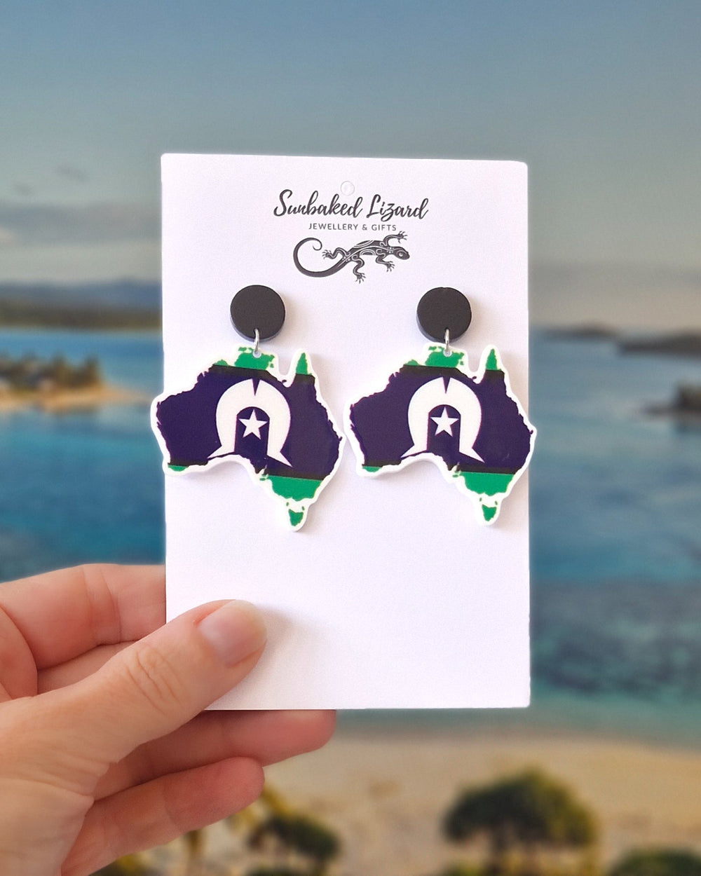 Australia Earrings - Torres Strait Island Flag on a white Sunbaked Lizard Jewellery & Gifts card held against an island background