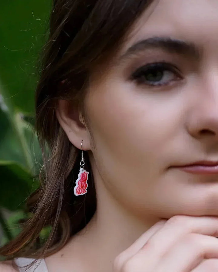 Close up of woman wearing bacon rasher earring with a blurred green background