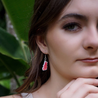 Close up of woman wearing bacon rasher earring with a blurred green background