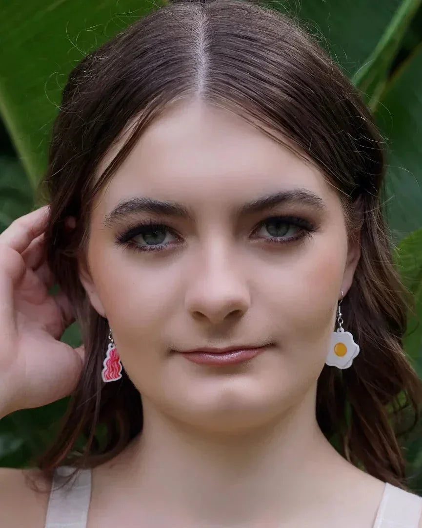 Woman with bacon and egg novelty earrings with green leaves in the background