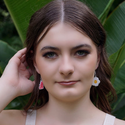 Woman with bacon and egg novelty earrings with green leaves in the background