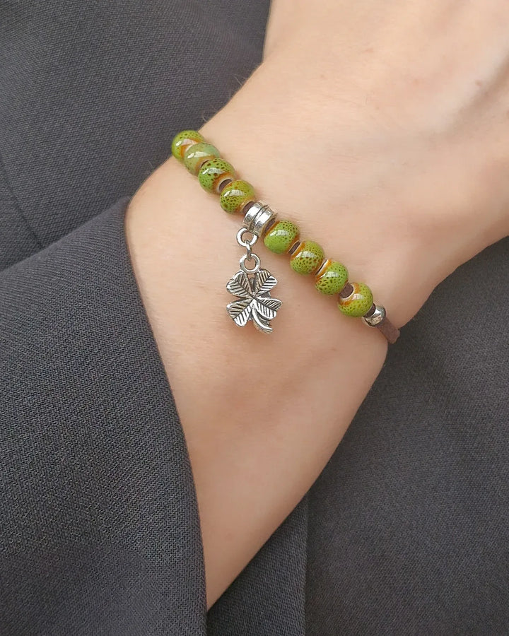 A shamrock charm bracelet with green beads and a silver four-leaf clover charm worn on a wrist