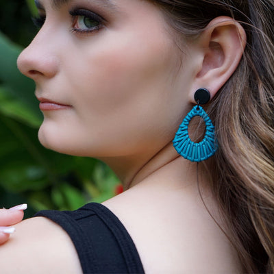 Woman wearing blue woven earrings with a blurred green background