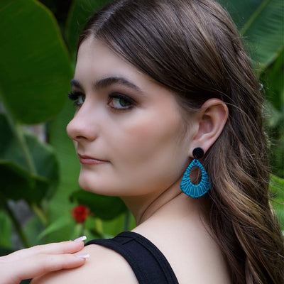 Woman looking back over her shoulder wearing blue earrings with a green leafy background