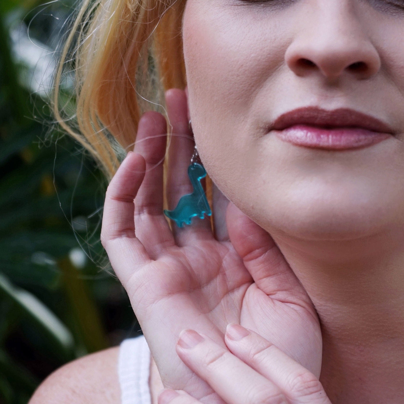 Woman wearing blue dinosaur earrings with a blurred green background