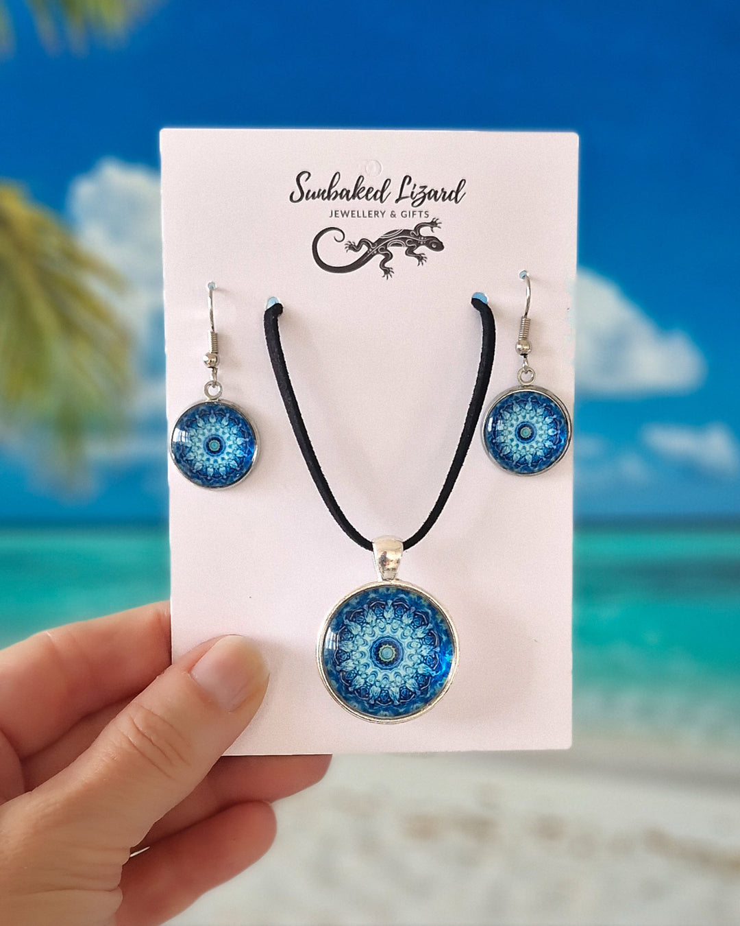 Blue Mandala necklace and matching drop earrings set on Sunbaked Lizard card with a tropical beach background