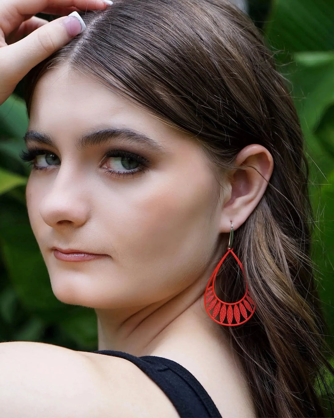 Model wearing bright orange Leafy Droplet Filigree Drop Earrings against green foliage