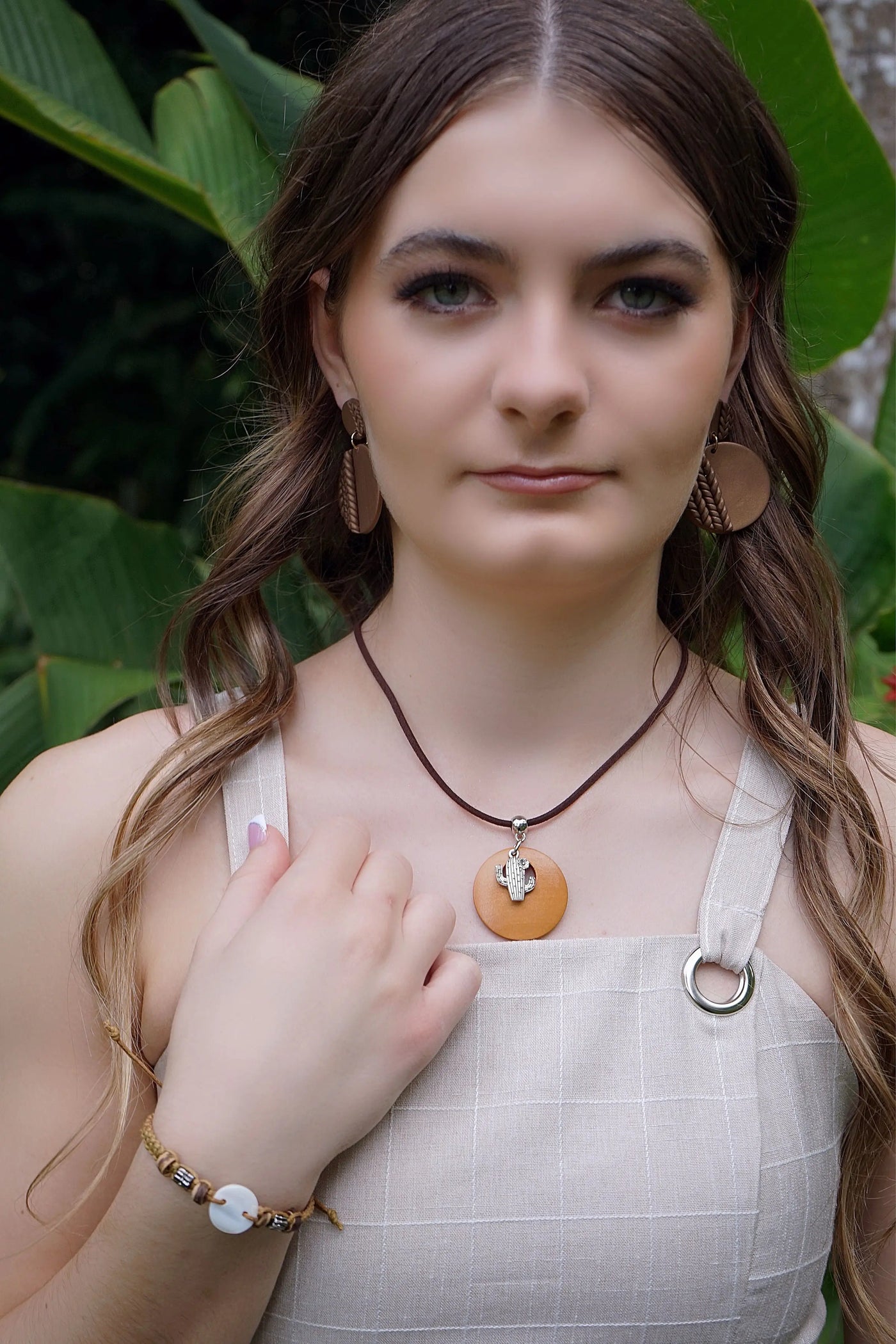 Woman wearing a necklace with a cactus pendant in front of green foliage