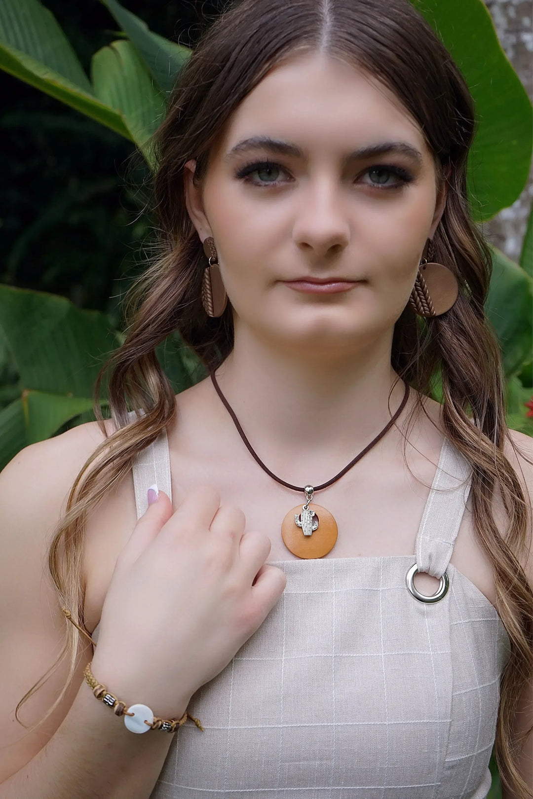 Woman wearing round patterned brown earrings in front of green foliage