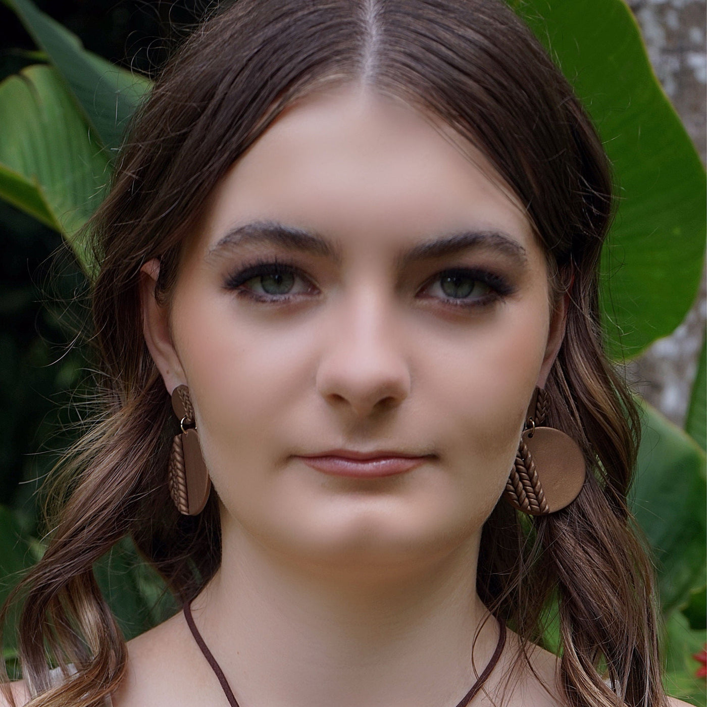 Woman wearing round patterned brown earrings in front of green foliage