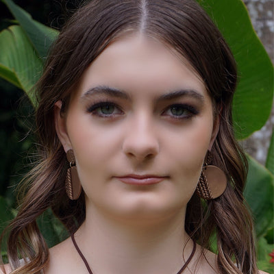 Woman wearing round patterned brown earrings in front of green foliage