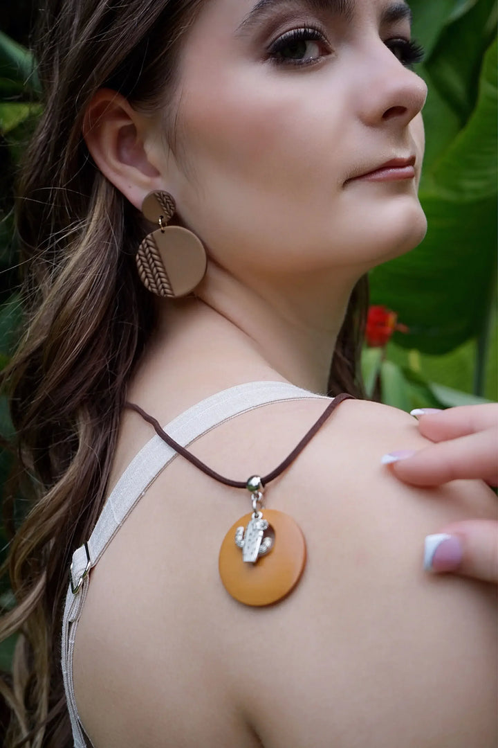 Woman wearing round clay earrings, surrounded by green foliage.