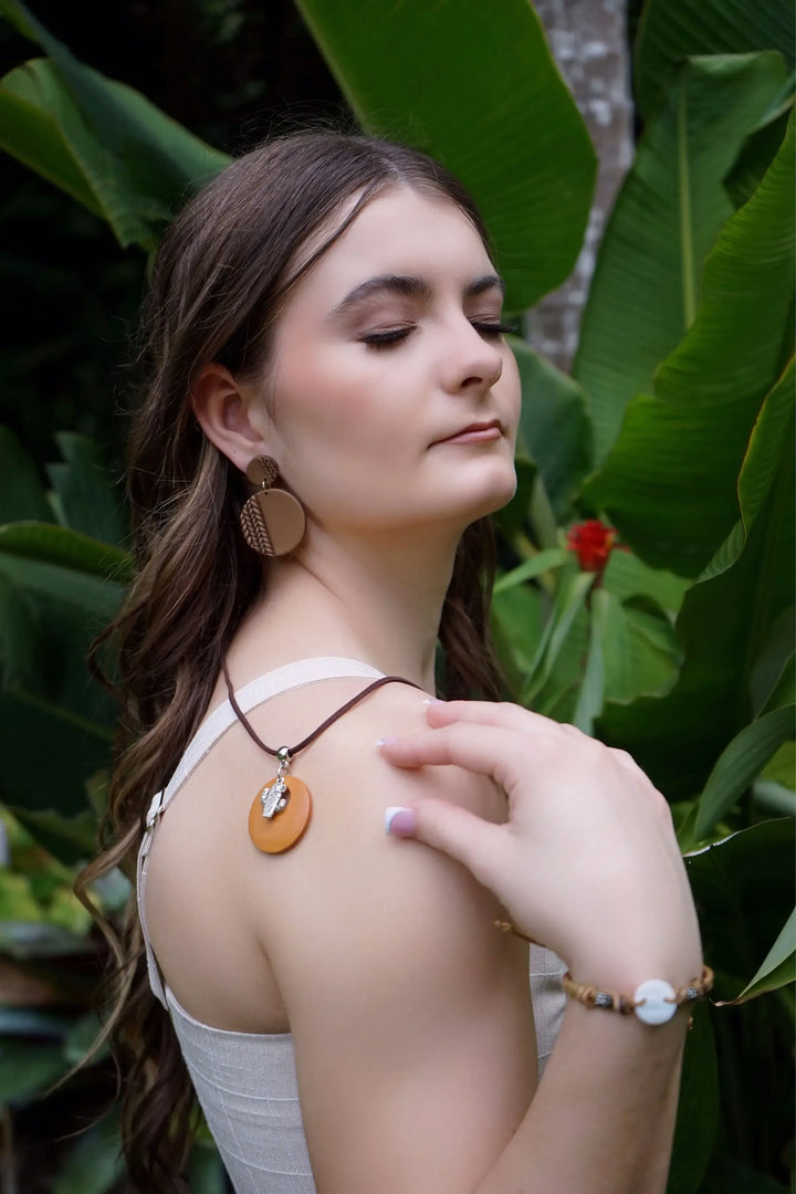 Woman with chocolate colour plaited earrings with bright green leaves in the background