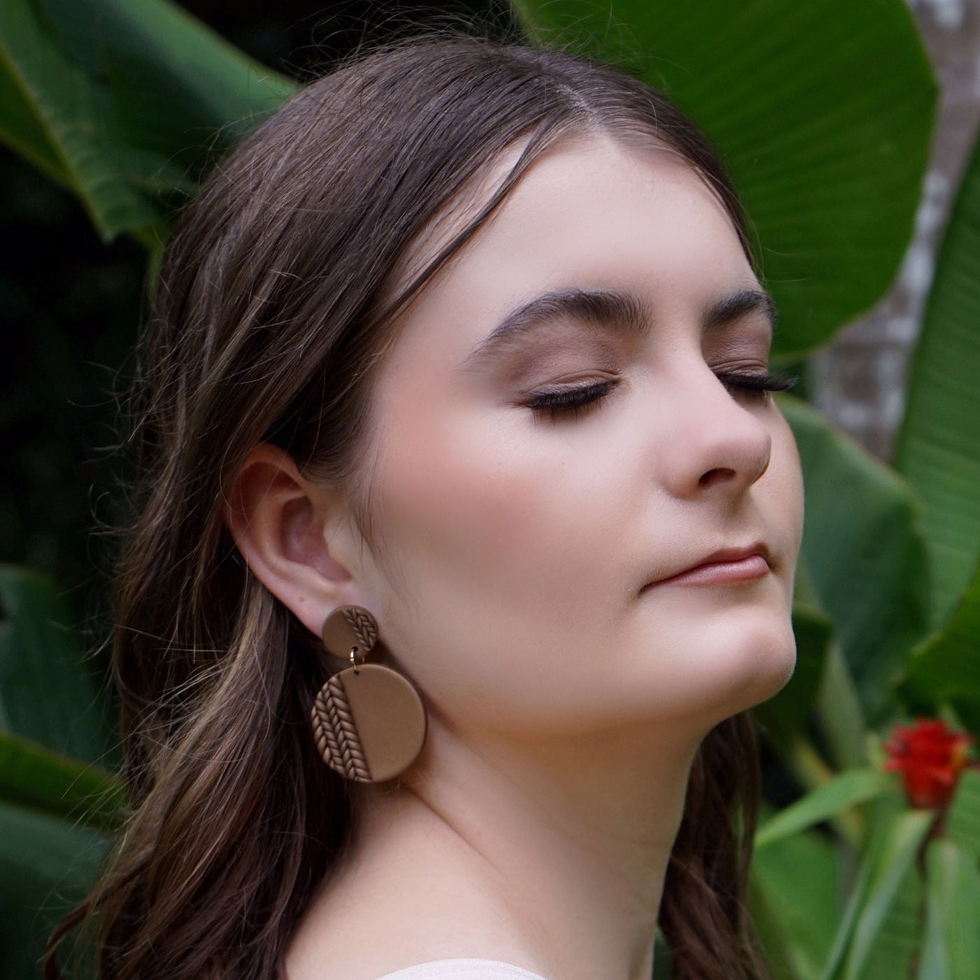 Woman with chocolate colour plaited earrings with bright green leaves in the background