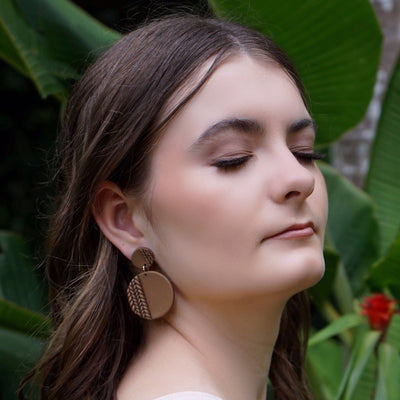 Woman with chocolate colour plaited earrings with bright green leaves in the background