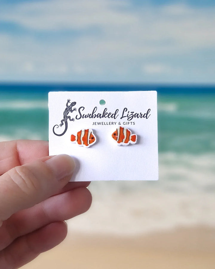 Card with clownfish earrings held by a hand against a beach background