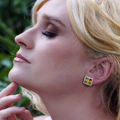 Woman with blonde hair and colourful  crayon earrings against a green leafy background