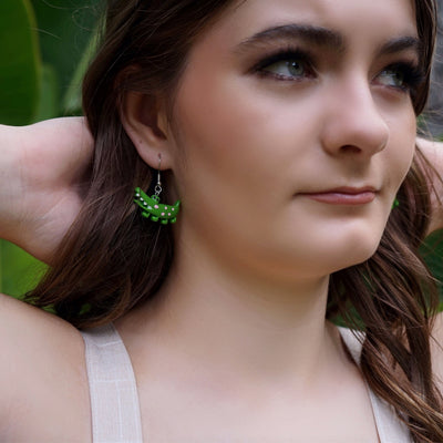 Close up view of woman with green crocodile earrings against a natural background