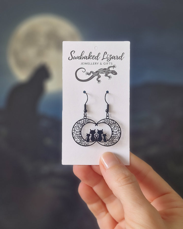 Hand holding Filigree Cats on the Moon Drops on a jewellery backing card to show scale