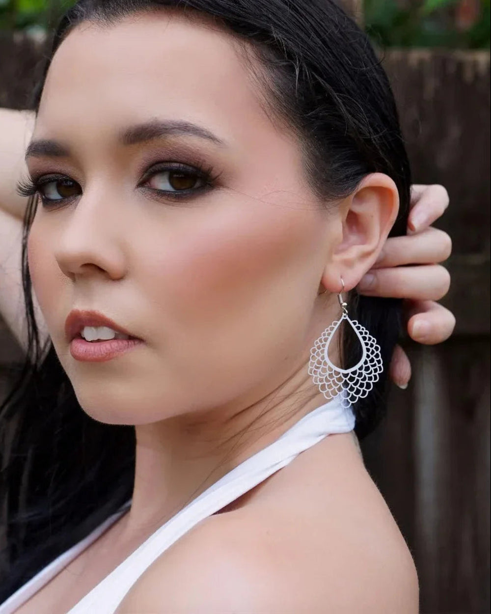 Side profile of model wearing long filigree teardrop dangle earrings with scalloped lace-style cut-out detail