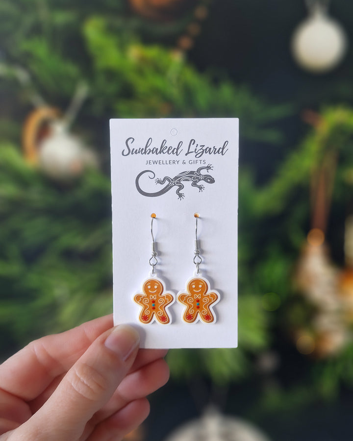 Picture of a hand holding Gingerbread Man Christmas earrings on a Sunbaked Lizard Jewellery &amp; Gifts backing card, showing scale