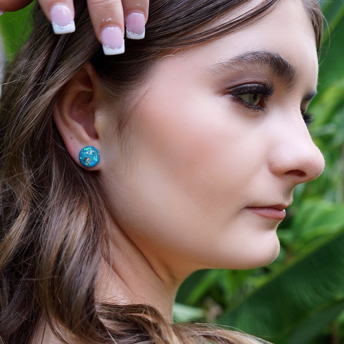 Woman with a blue earring in front of green foliage
