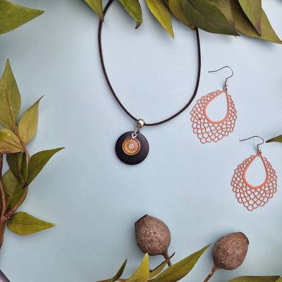 Jewelry set with earrings and necklace on a light surface surrounded by green leaves with matching earrings.