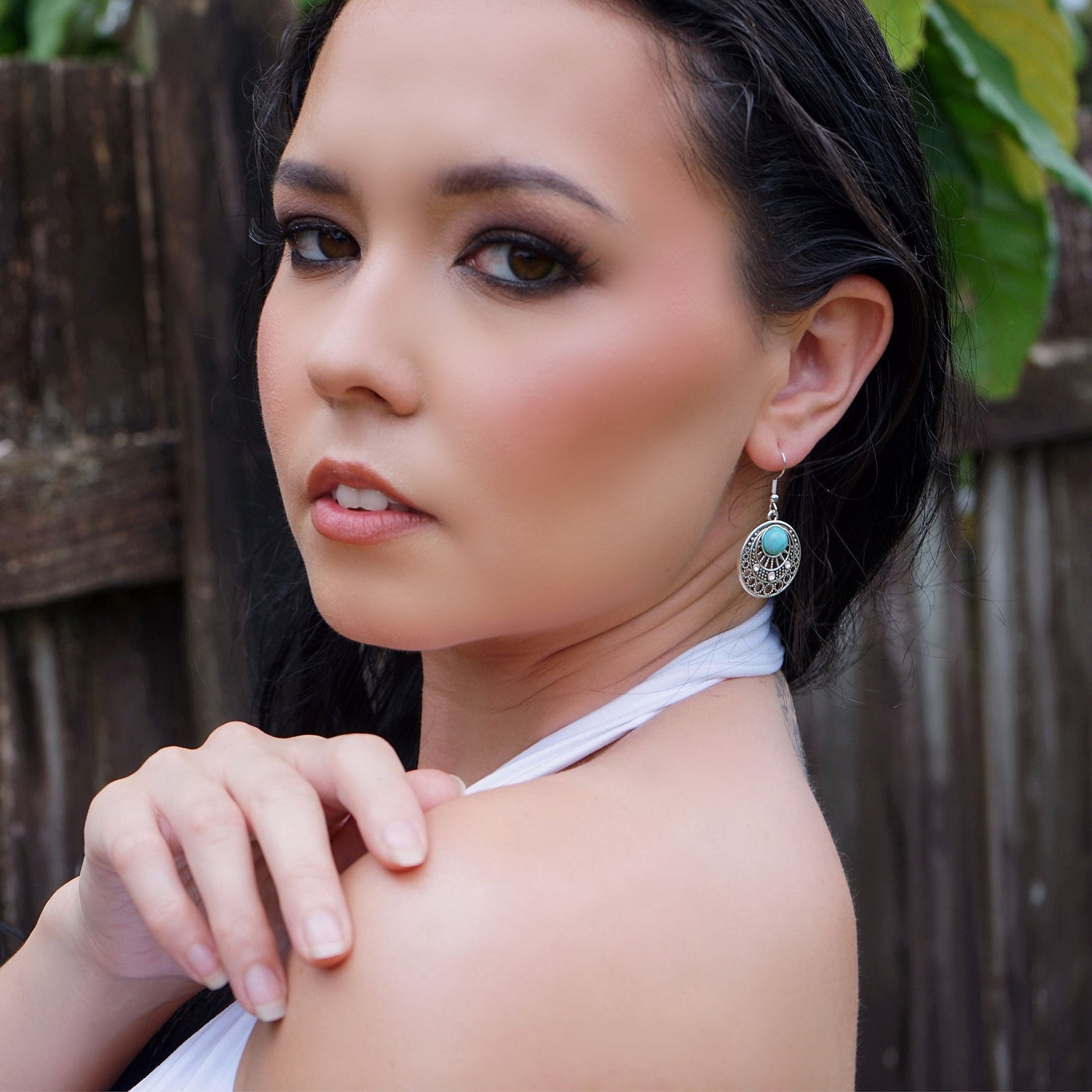 Woman with dark hair and silver turquoise earrings against a wooden fence background