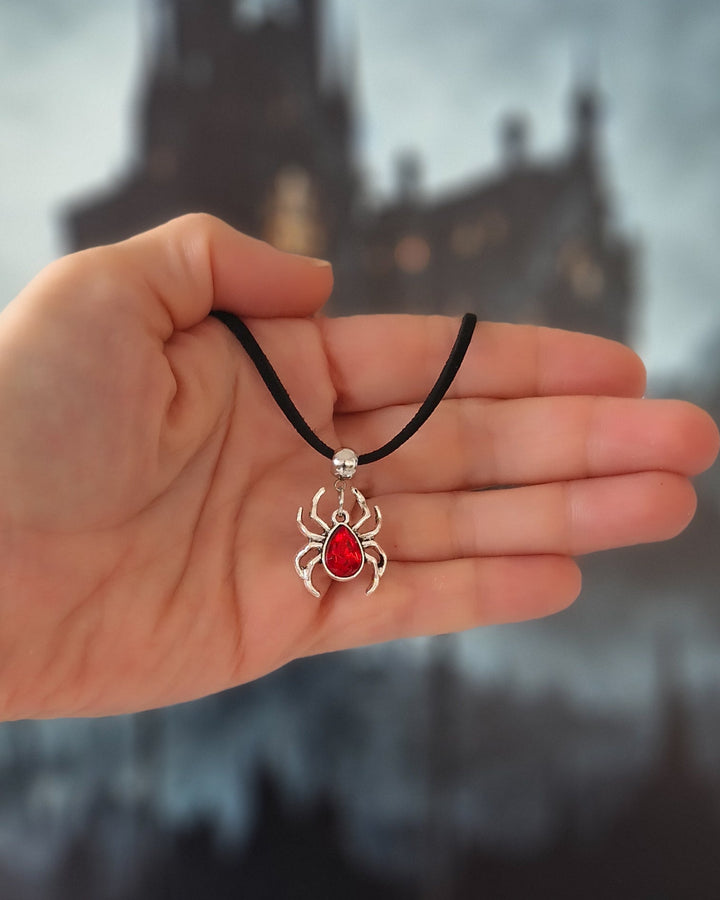 Hand holding a necklace with a silver spider pendant against a blurred gothic castle background