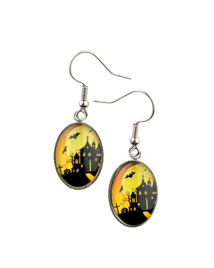 Glass oval haunted house earrings showing manor silhouette, bats and graveyard against amber moon, silver hooks