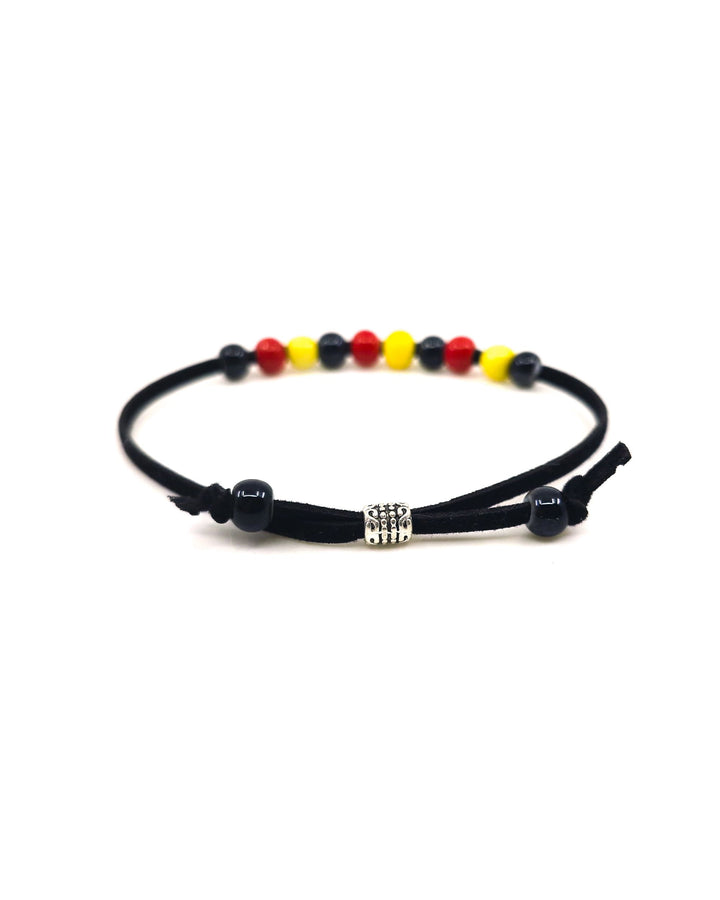Close up of adjuster bead on an indigenous inspired bracelet with red, yellow, and black ceramic beads on a white background
