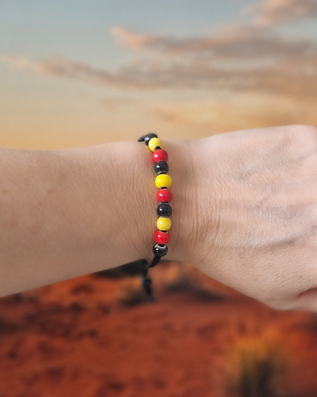 Indigenous inspired bracelet with red, yellow, and black ceramic beads on a wrist with a red desert background.