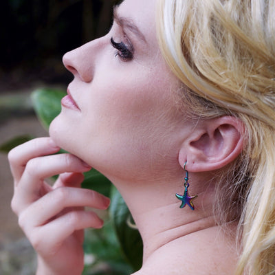 Close-up of a woman wearing starfish earrings with a blurred natural background