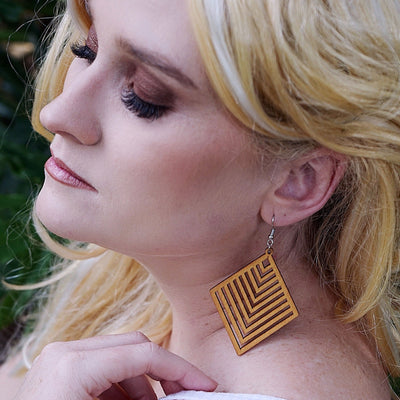Woman with blonde hair and large timber geometric earrings against a blurred natural background