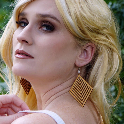 Woman with blonde hair and large timber diamond earrings standing in a forest setting