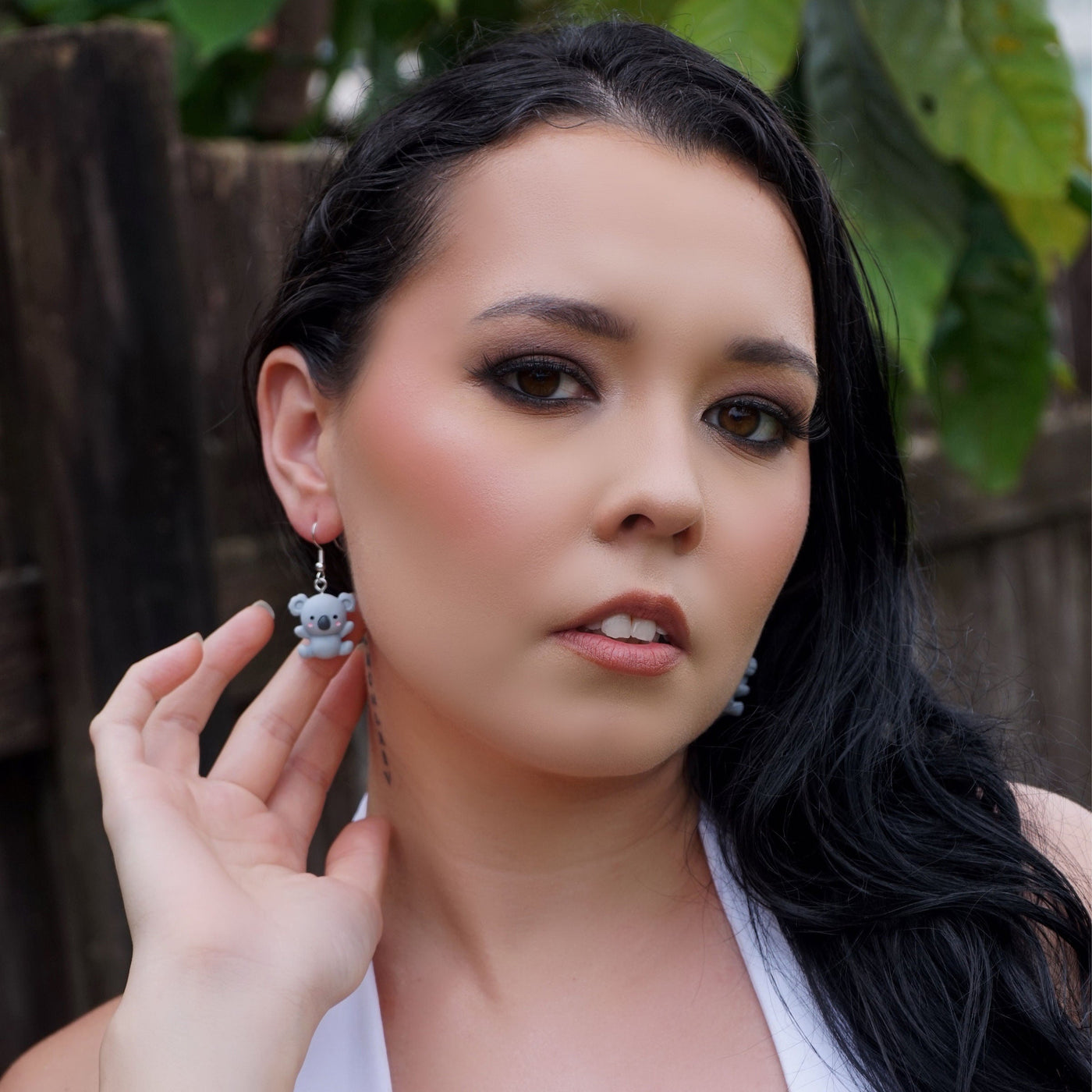 Woman wearing koala earrings in front of a green leafy background
