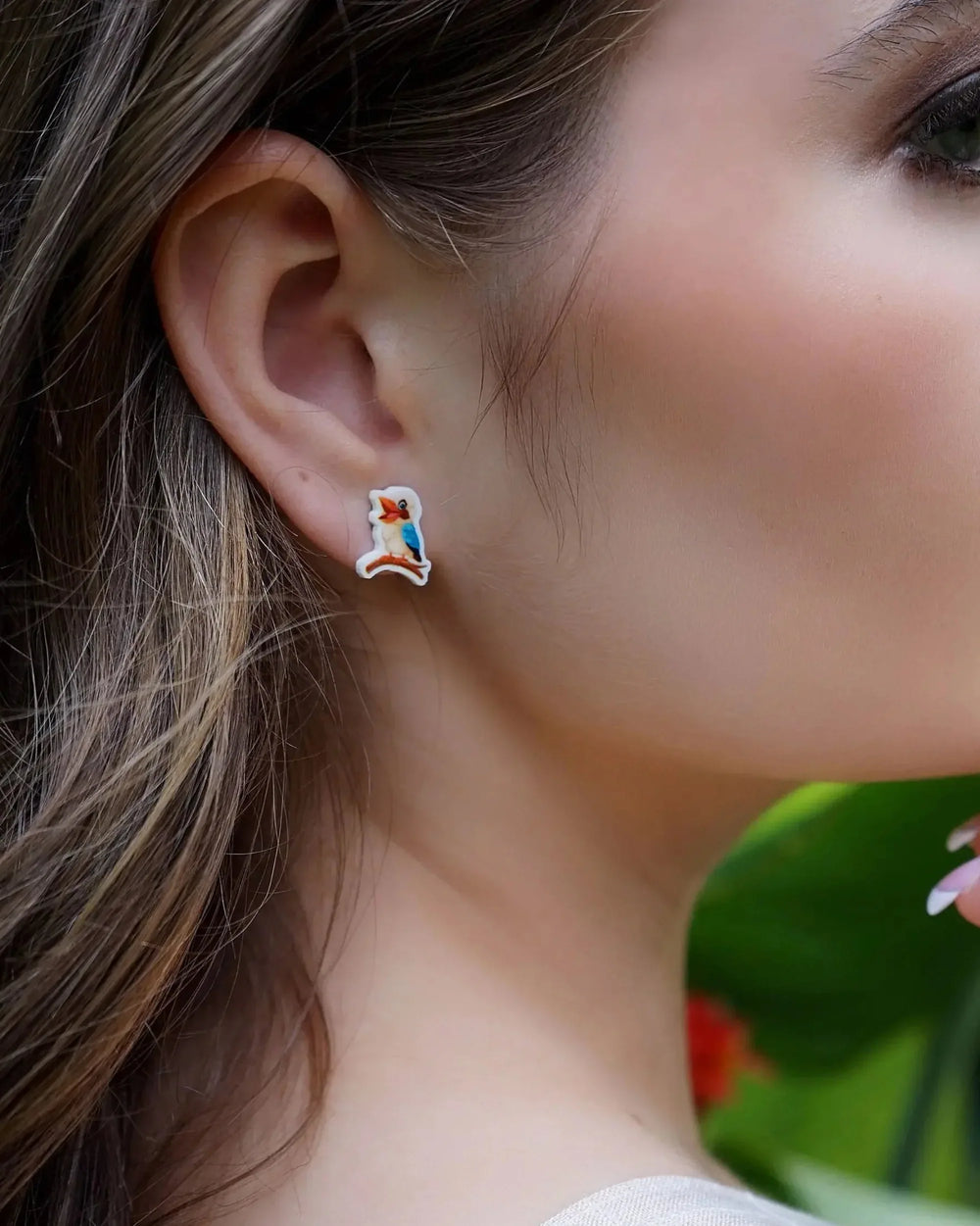 Close-up of a woman wearing kookaburra stud earrings with blurred garden in the background