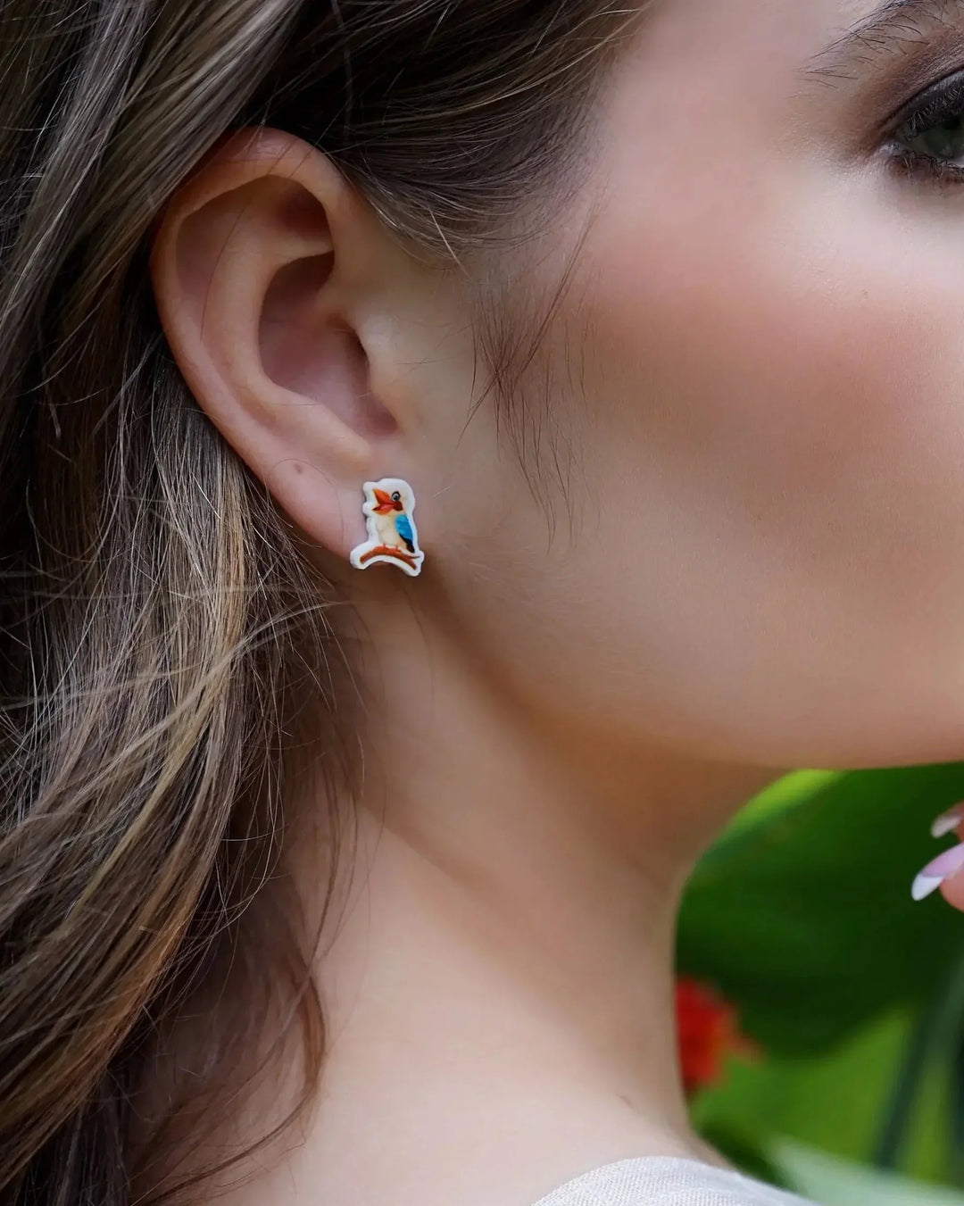 Close-up of a woman wearing kookaburra stud earrings with blurred garden in the background