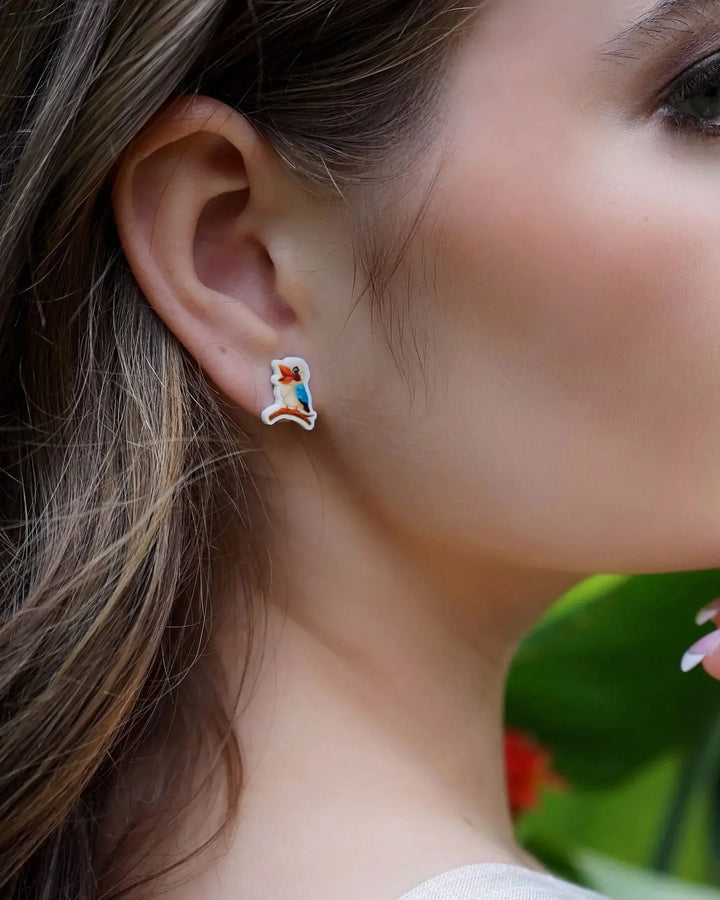 Close-up of a woman wearing kookaburra stud earrings with blurred garden in the background